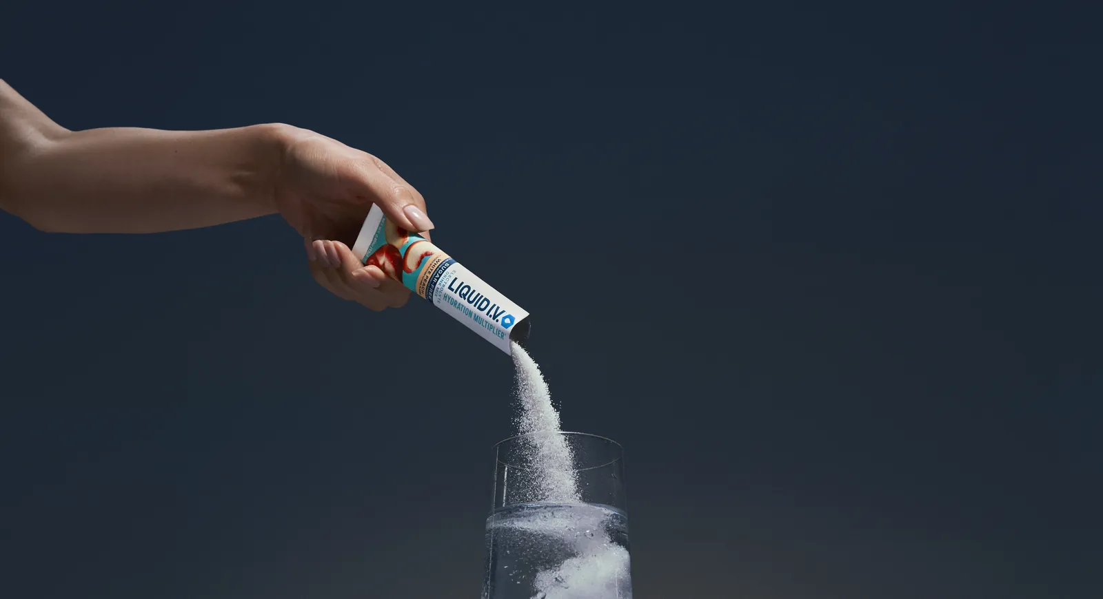 Liquid I.V. hydration multiplier being poured into a glass of water in Green House product photography.